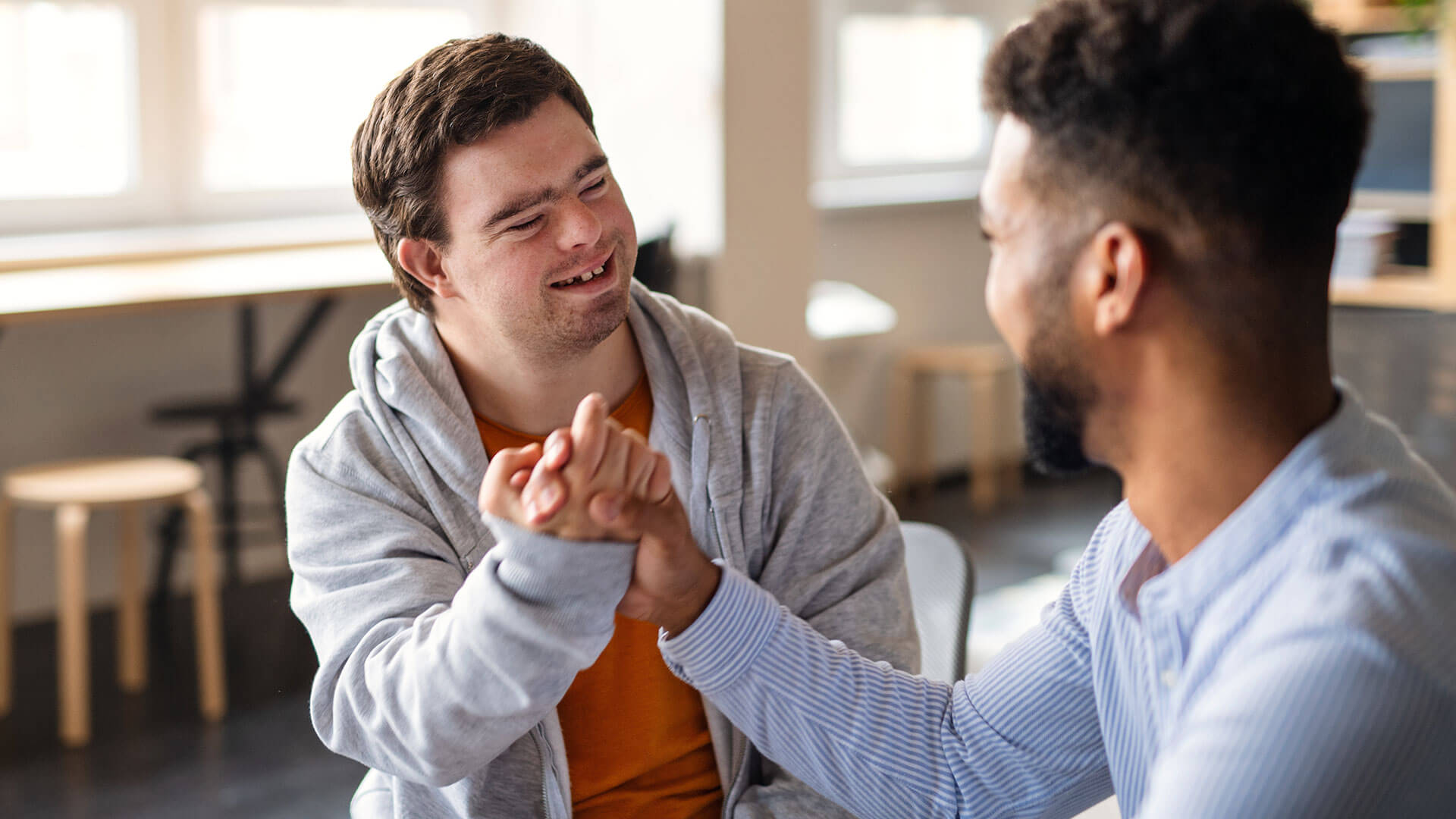 Support worker and NDIS participant sharing a warm, joyful handshake during a support session