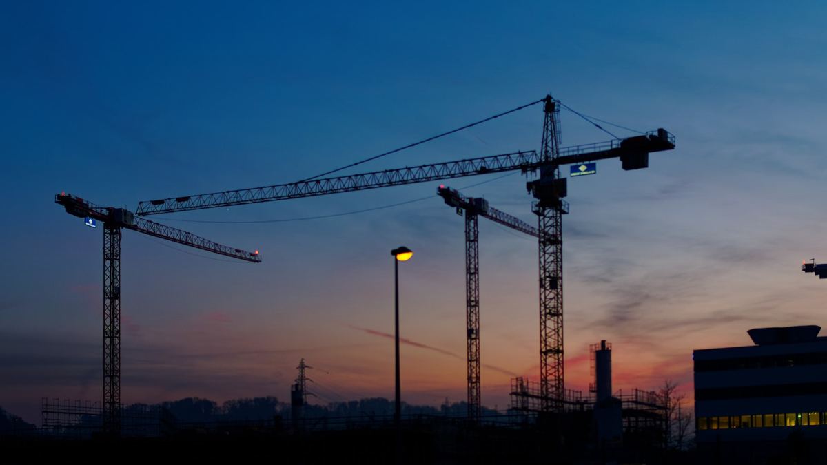 Tower cranes silhouetted against an evening sky